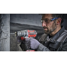 Artisan utilisant une perceuse visseuse à percussion sans fil Einhell pour percer un mur en béton, portant lunettes et protection auditive.