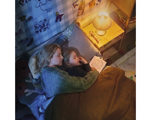 Mère et enfant lisant ensemble un livre dans la chambre à coucher sous la lumière chaleureuse d une lampe de chevet.