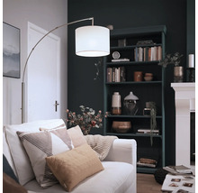 Lampadaire arc moderne avec abat-jour en tissu et structure en métal dans un salon confortable avec bibliothèque et cheminée.