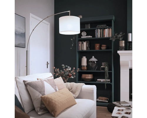 Lampadaire arc moderne avec abat-jour en tissu et structure en métal dans un salon confortable avec bibliothèque et cheminée.