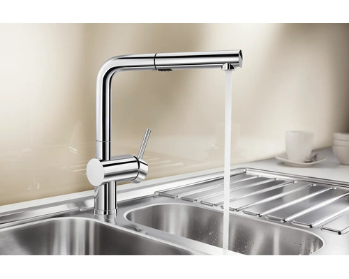 Mitigeur de cuisine moderne en métal avec douchette extractible et eau courante au-dessus d un évier en acier inoxydable.