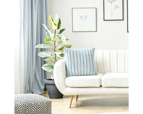 Un coussin douillet nervuré sur un canapé clair dans un salon lumineux avec une plante et un pouf géométrique.