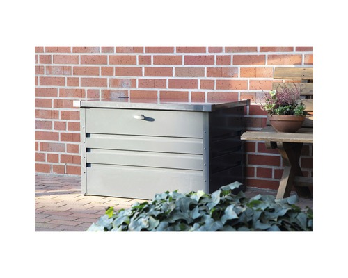 Coffre de jardin gris en métal devant un mur de briques.