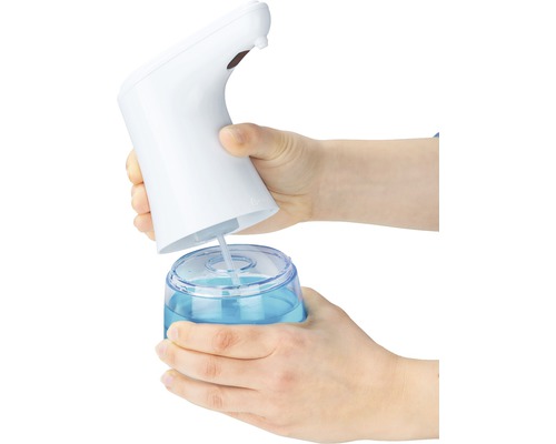 Des mains remplissent un distributeur de savon sans contact avec du savon liquide