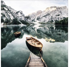 Ein See mit zwei Booten und einem Holzsteg vor einer Berglandschaft.