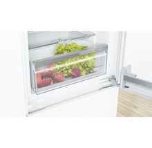 Geöffneter Kühlschrank mit Gemüsefach gefüllt mit Salat und Pfirsichen.