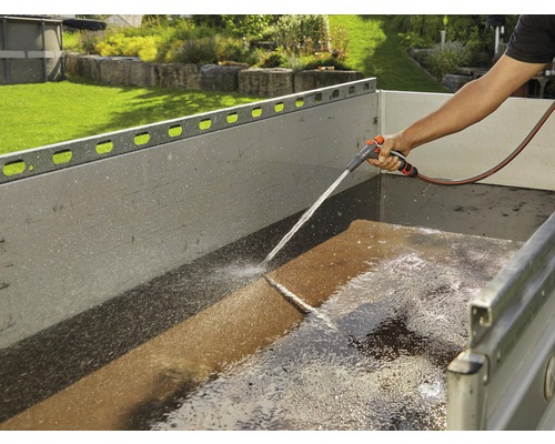 Eine Person reinigt einen Anhänger mit einem Gartenschlauch.