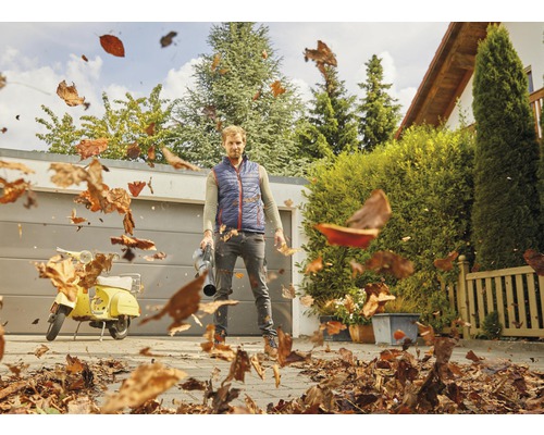 Mann benutzt einen Laubbläser, um Blätter auf einem Hof zu entfernen.
