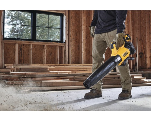 Un homme utilise un souffleur à feuilles sans fil jaune et noir DeWalt sur un chantier.