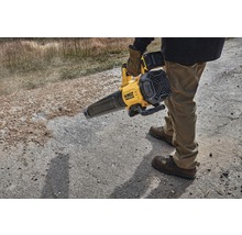 Une personne utilise un souffleur à feuilles sans fil DeWalt jaune sur une surface non pavée.