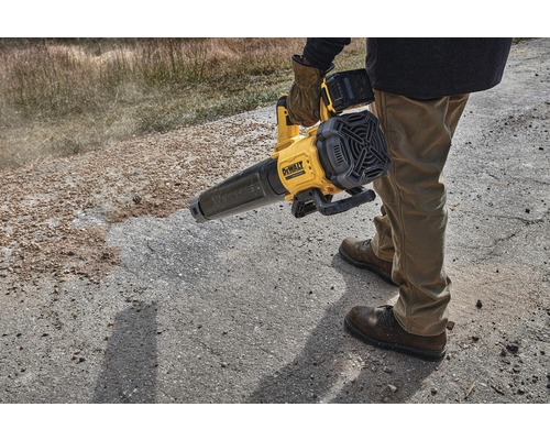 Une personne utilise un souffleur à feuilles sans fil DeWalt jaune sur une surface non pavée.