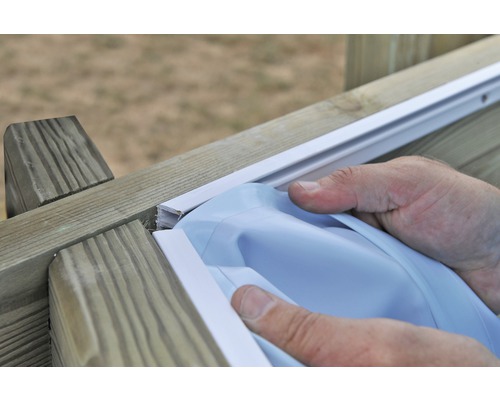 Une personne fixe une bâche de piscine sur un cadre en bois.