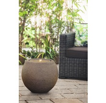 Fontaine sphérique décorative en pierre à côté d''un fauteuil en rotin dans le jardin
