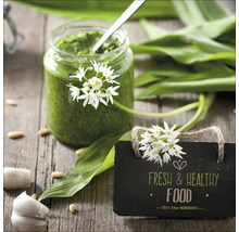 Einmachglas mit Bärlauchpesto, Bärlauchblätter, Knoblauchzehen und Schild mit dem Text frische und gesunde Lebensmittel auf einem Holztisch