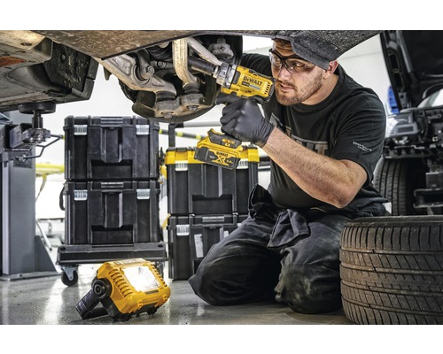 Un mécanicien travaille sur une voiture avec une clé à chocs à batterie, avec des boîtes à outils et une lampe de travail en arrière-plan.