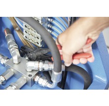Hand, die mit einer Zange an einer Hydraulikleitung arbeitet
