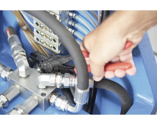 Main travaillant sur une conduite hydraulique avec une pince