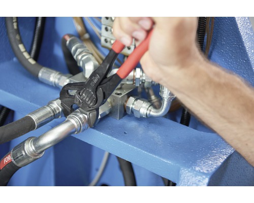 Une personne utilise une pince multiprise sur un raccord hydraulique.