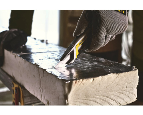 Eine Hand mit Schutzhandschuh schneidet mit einem Universalmesser eine Isolierplatte.