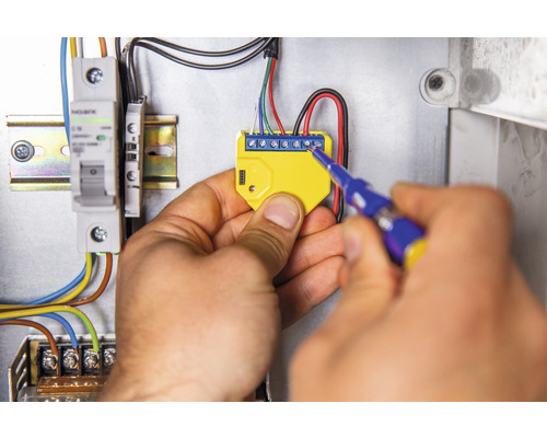 Elektriker montiert elektronisches Bauteil mit Schraubenzieher in Verteilerkasten