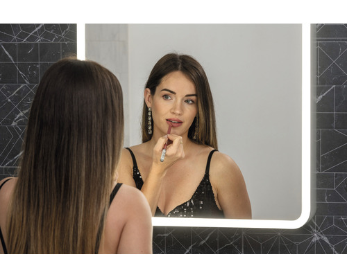 Frau trägt Lippenstift vor einem beleuchteten Spiegel im Badezimmer