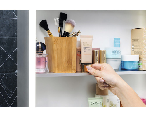 Scène de salle de bains avec des produits cosmétiques, des pinceaux de maquillage dans un récipient et une main tenant une boîte.