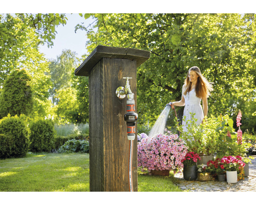 Frau giesst Blumen mit einem Gartenschlauch an einem Wasserhahn im Garten