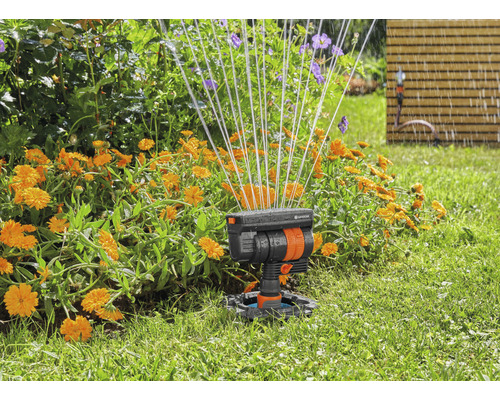 Gartenszene mit Rasensprenger im Einsatz zur Bewässerung von Blumen