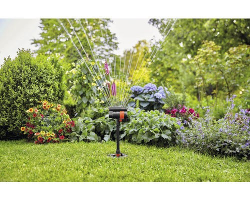Gartensprenger im Einsatz auf Rasenfläche mit Blumenbeeten im Hintergrund.