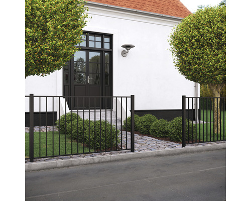 Clôture métallique noire devant une maison avec des arbres et un chemin pavé