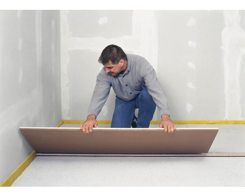 Ein Mann verlegt eine Dämmplatte auf einer Fußbodenheizung in einem Raum.