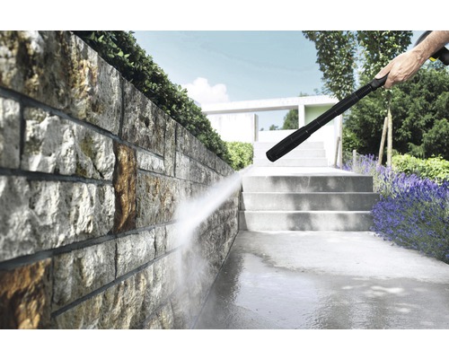 Nettoyeur haute pression en action pour nettoyer un mur en pierre et une allée