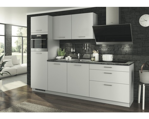 Cuisine moderne avec armoires blanches, four encastré et hotte aspirante devant un mur en pierre sombre.