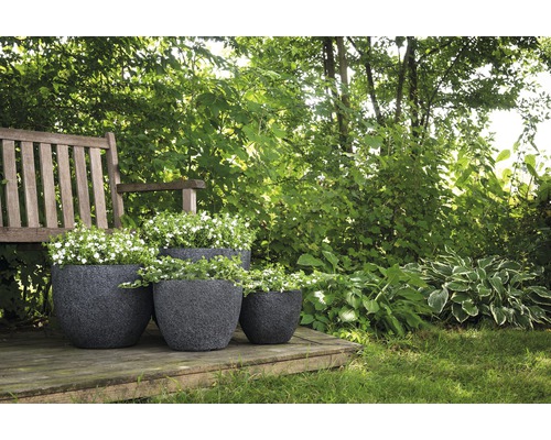 Trois jardinières sombres en plastique plantées sur une terrasse en bois dans un jardin.