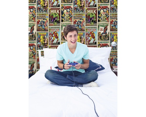 Adolescent assis sur un lit avec une manette de jeu vidéo devant un papier peint de bande dessinée