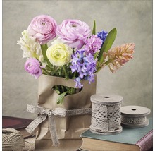 Bouquet de renoncules et de jacinthes dans un sac en papier avec de la dentelle, entouré de bobines de fil et de livres