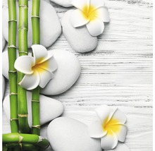 Arrangement décoratif avec tiges de bambou, pierres blanches et fleurs de frangipanier sur une table en bois.