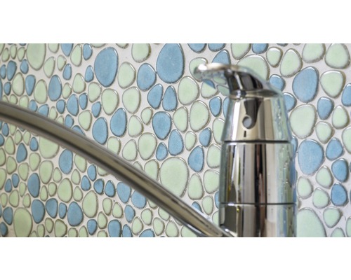 Nahaufnahme eines Wasserhahns vor einer Wand mit Mosaikfliesen in Kieselmuster
