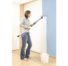 Femme peint un mur avec un rouleau de peinture et un manche télescopique