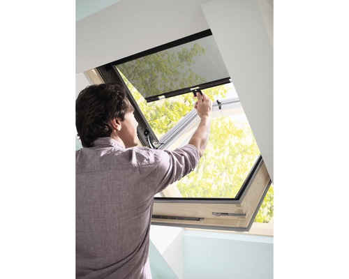 Mann bedient ein Dachfenster mit Insektenschutz