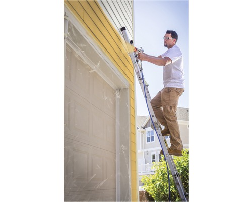 Homme sur une échelle peignant le mur d''une maison avec un pulvérisateur de peinture