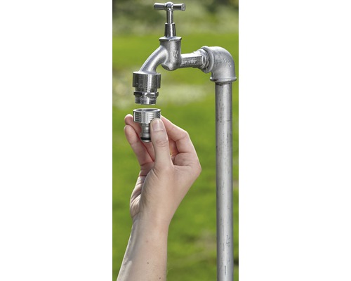 Une main monte un raccord de tuyau sur un robinet d''arrosage dans le jardin.