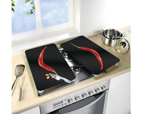 Deux plaques de recouvrement de cuisinière avec un motif de piment sur une cuisinière, avec des ustensiles de cuisine et une casserole à proximité.