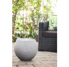Dekorativer Kugelbrunnen aus Stein auf einer Terrasse neben einem Rattansessel