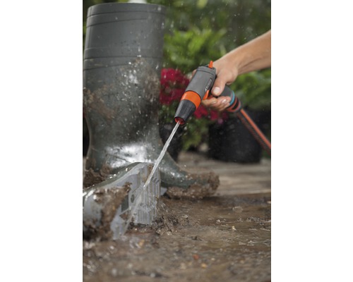 Eine Person reinigt eine Gartenschaufel mit einer Gartendusche neben Gummistiefeln.