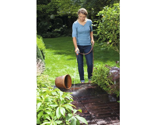 Frau bewässert mit einem Gartenschlauch eine Terrasse und eine Blumenvase im Garten.