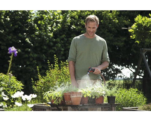 Ein Mann giesst Pflanzen in Töpfen mit einem Gartenschlauch im Garten.