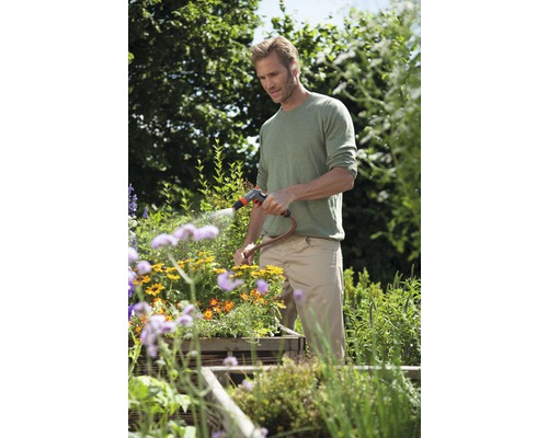 Mann bewässert Blumen mit Gartenschlauch im Garten.