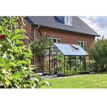 Gewächshaus aus Glas und Metall im Garten vor einem Backsteinhaus.