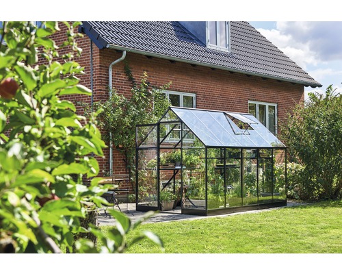 Gewächshaus aus Glas und Metall im Garten vor einem Backsteinhaus.